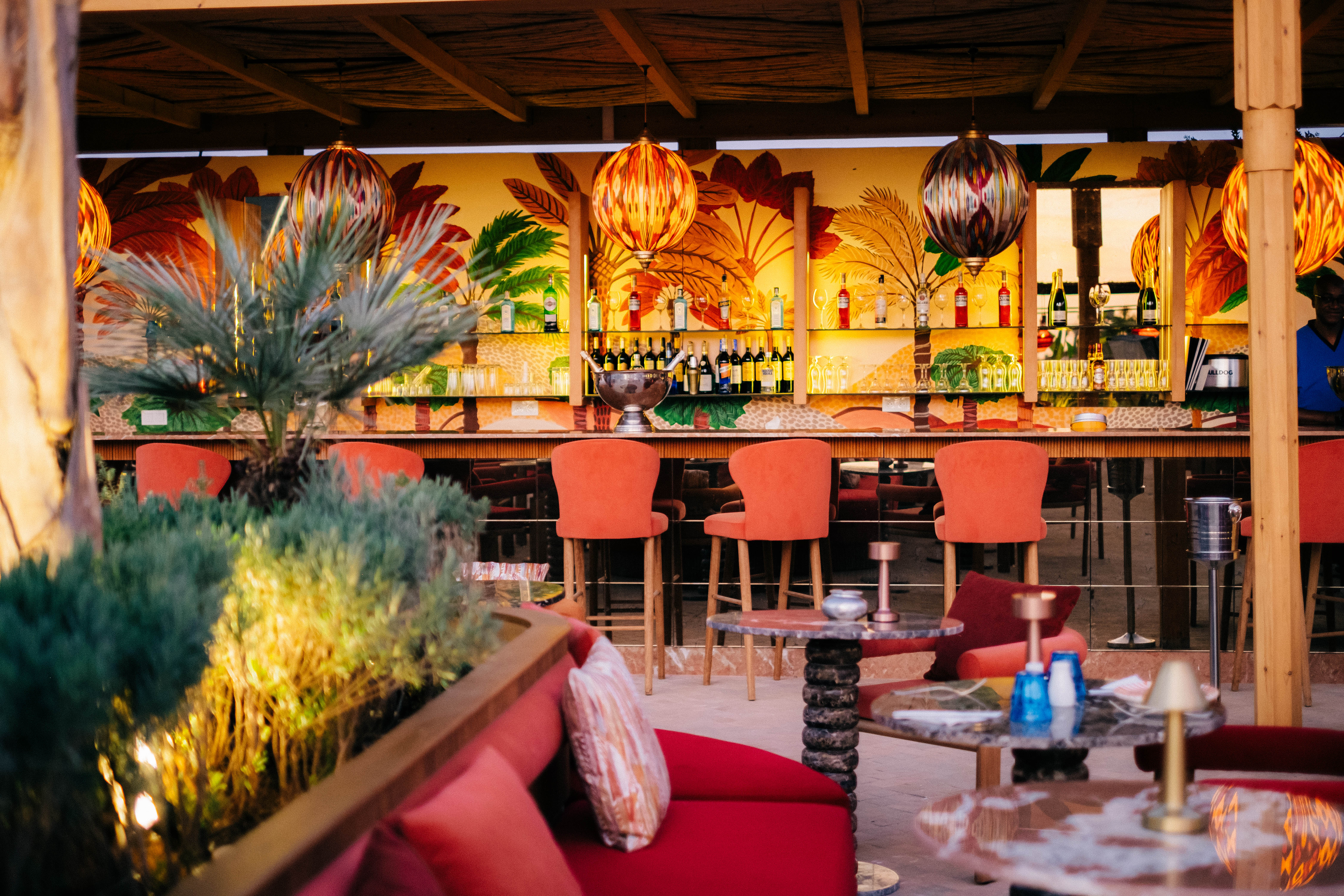 Stunning rooftop bar in Marrakech at sunset, with panoramic views of the Atlas mountains, stylish lounge furniture, infinity pool, and vibrant ambiance