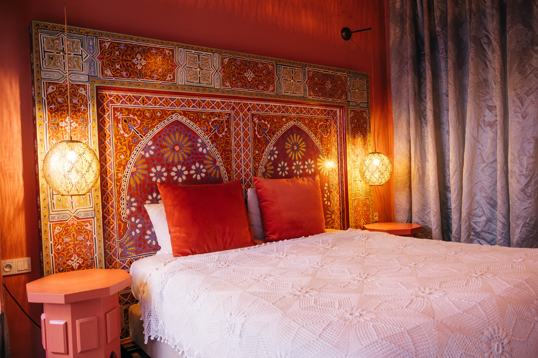 Moroccan comfort room bedroom area with traditional bed, warm textiles, carved wood headboard, soft lighting, cozy atmosphere