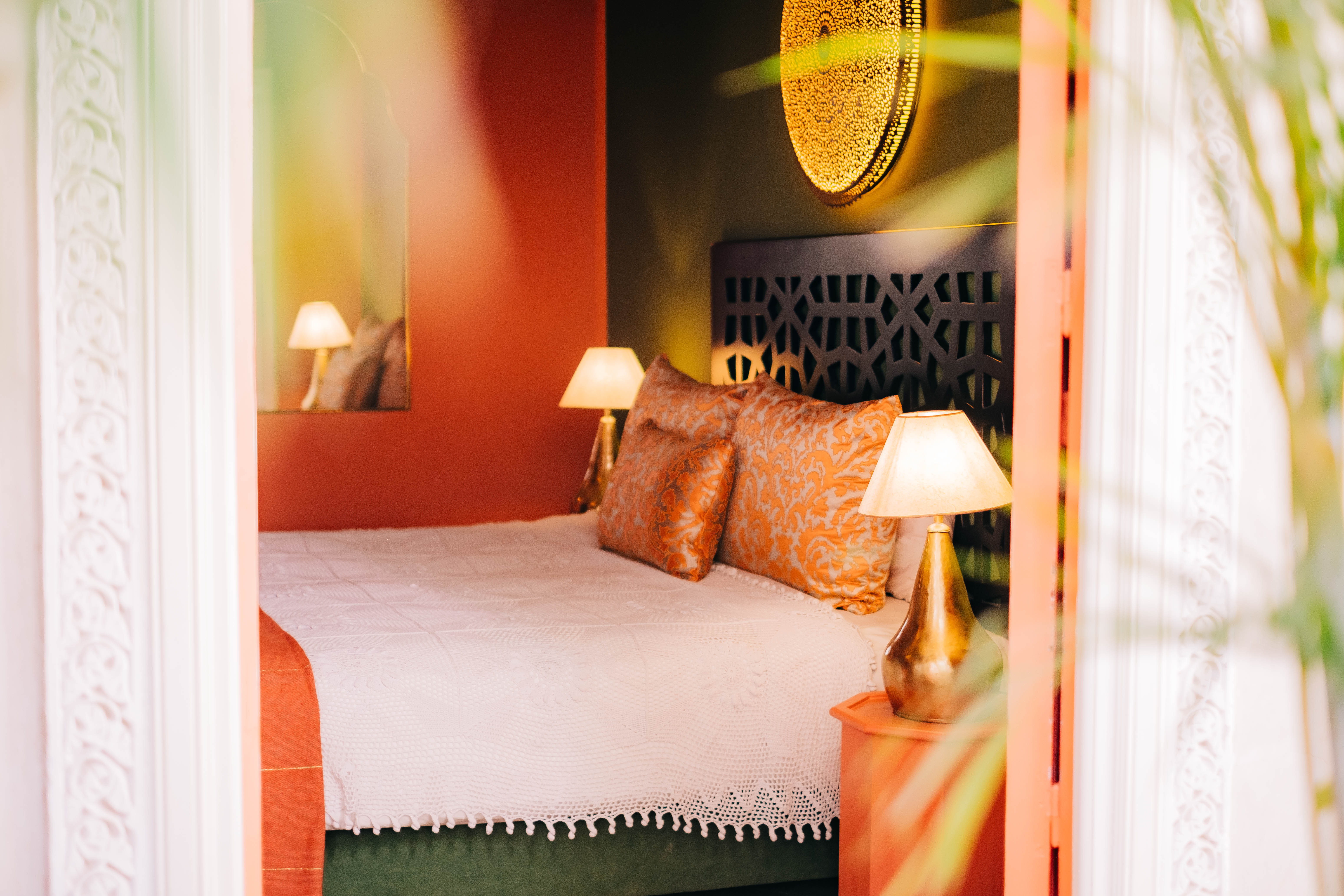 Moroccan comfort room bedroom area with traditional bed, warm textiles, carved wood headboard, soft lighting, cozy atmosphere