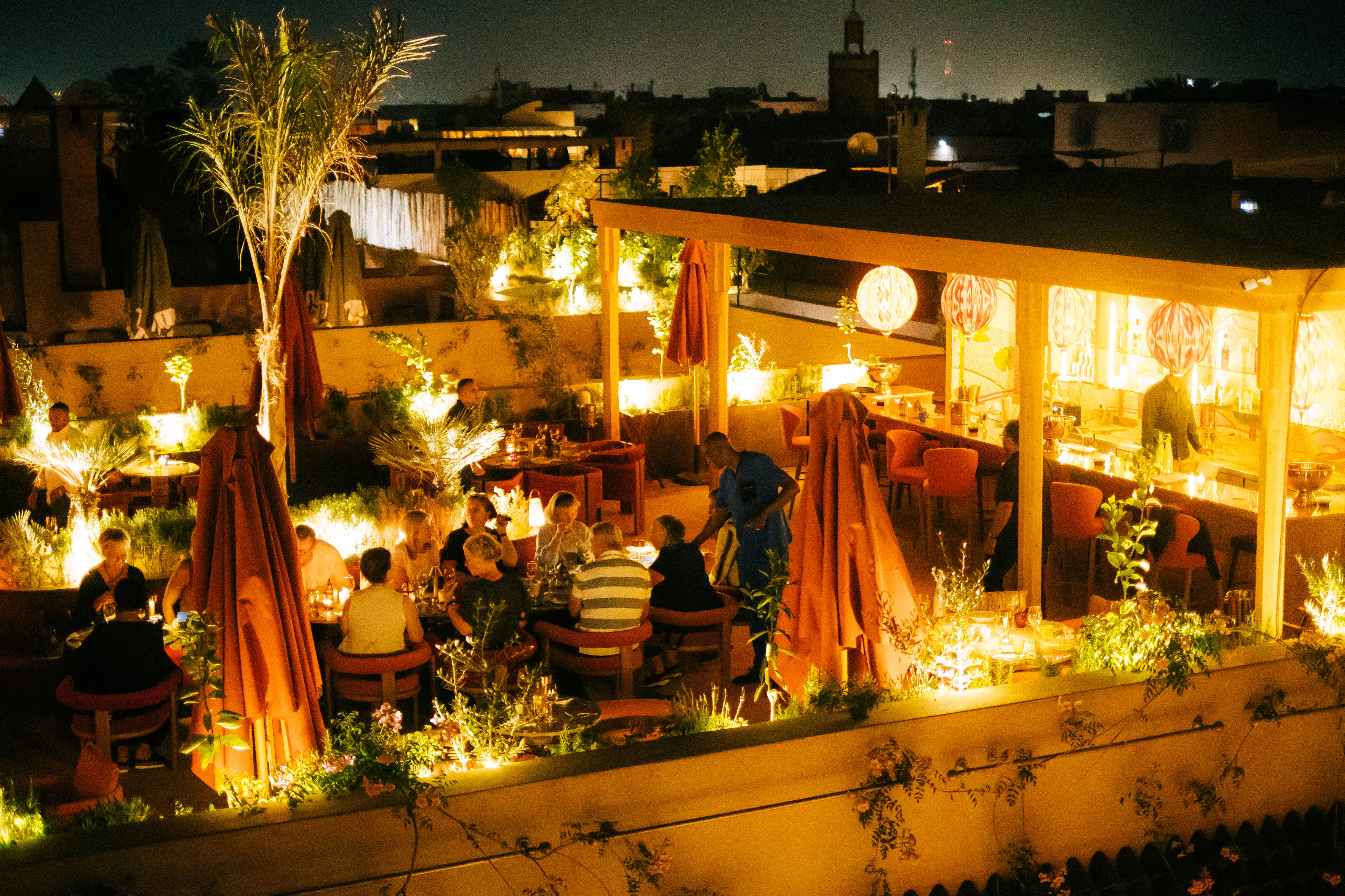 Close-up of a luxurious Moroccan bedroom detail, showing a carved wooden nightstand, elegant lamp, and rich textiles, moody lighting