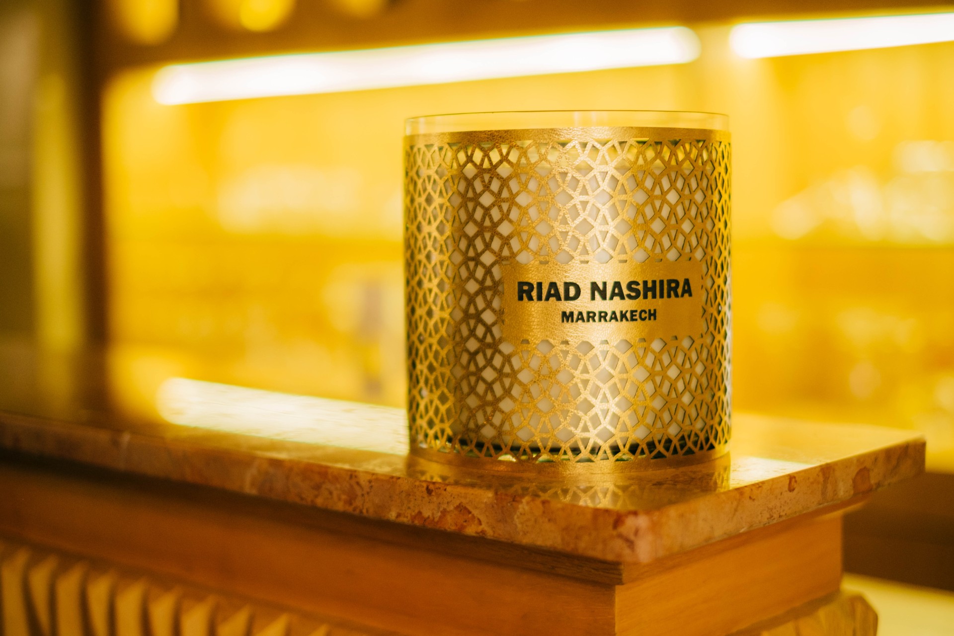 Close-up of a luxurious Moroccan bedroom detail, showing a carved wooden nightstand, elegant lamp, and rich textiles, moody lighting