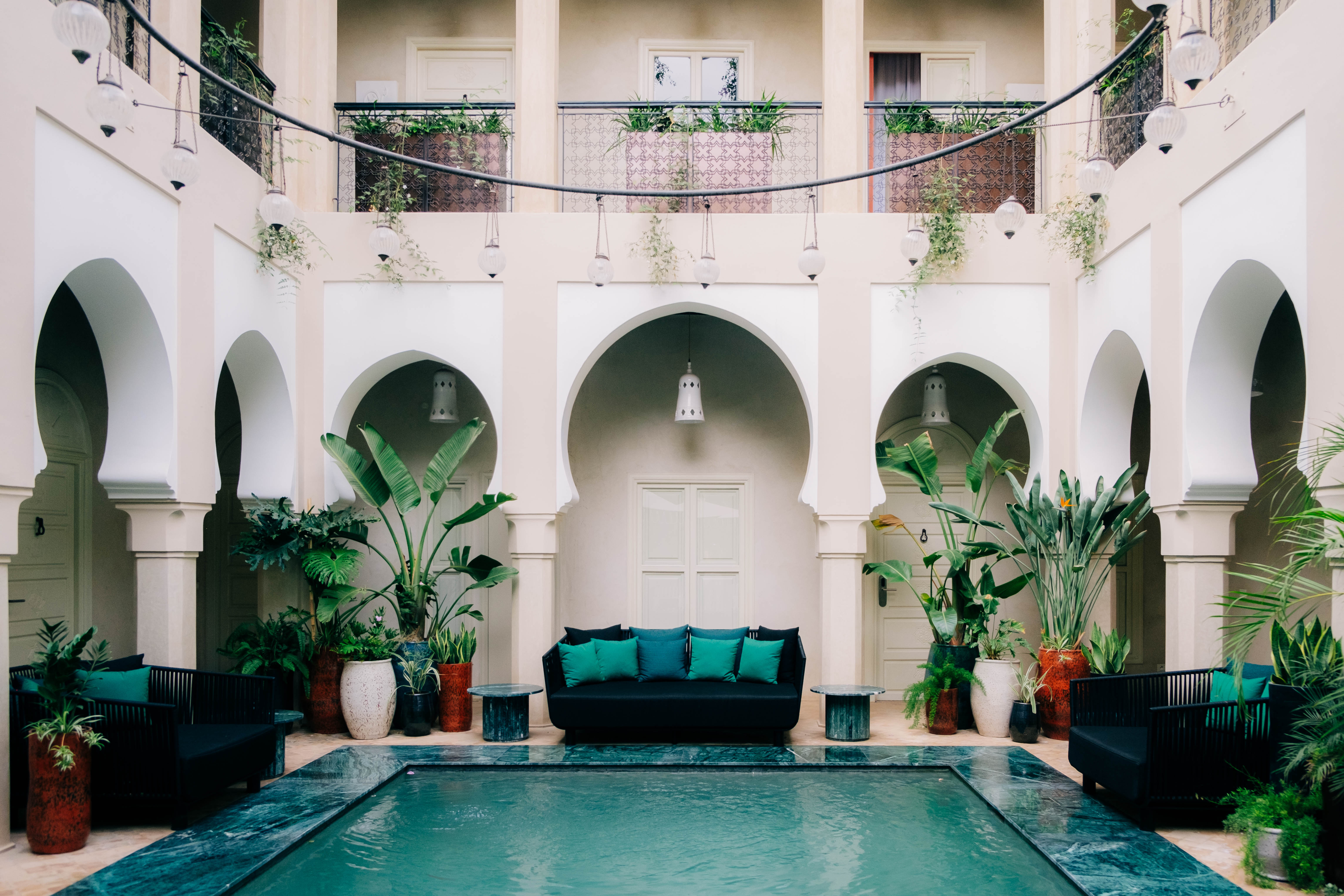 Close-up of a luxurious Moroccan bedroom detail, showing a carved wooden nightstand, elegant lamp, and rich textiles, moody lighting