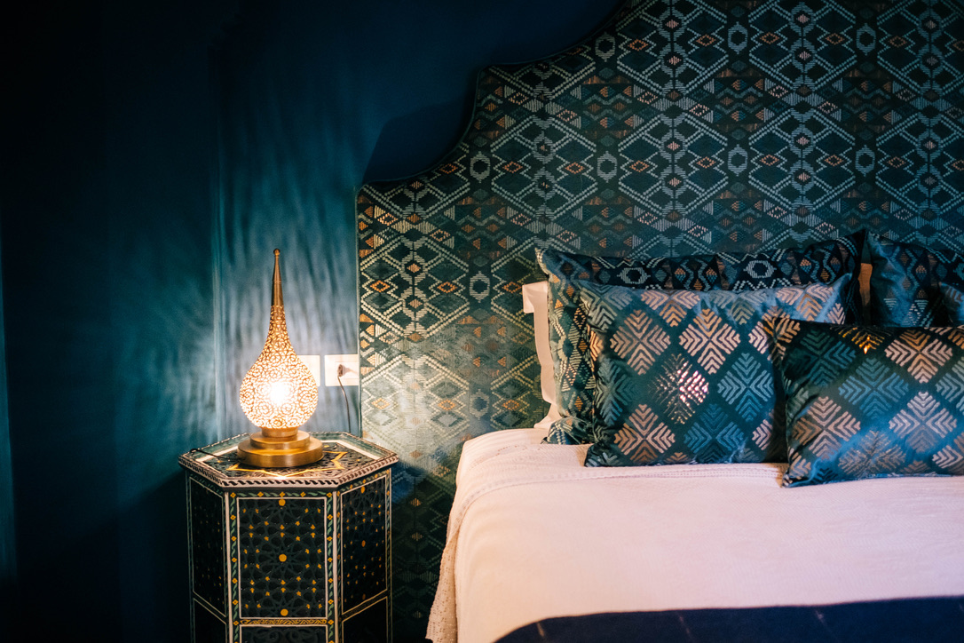 Moroccan comfort room bedroom area with traditional bed, warm textiles, carved wood headboard, soft lighting, cozy atmosphere